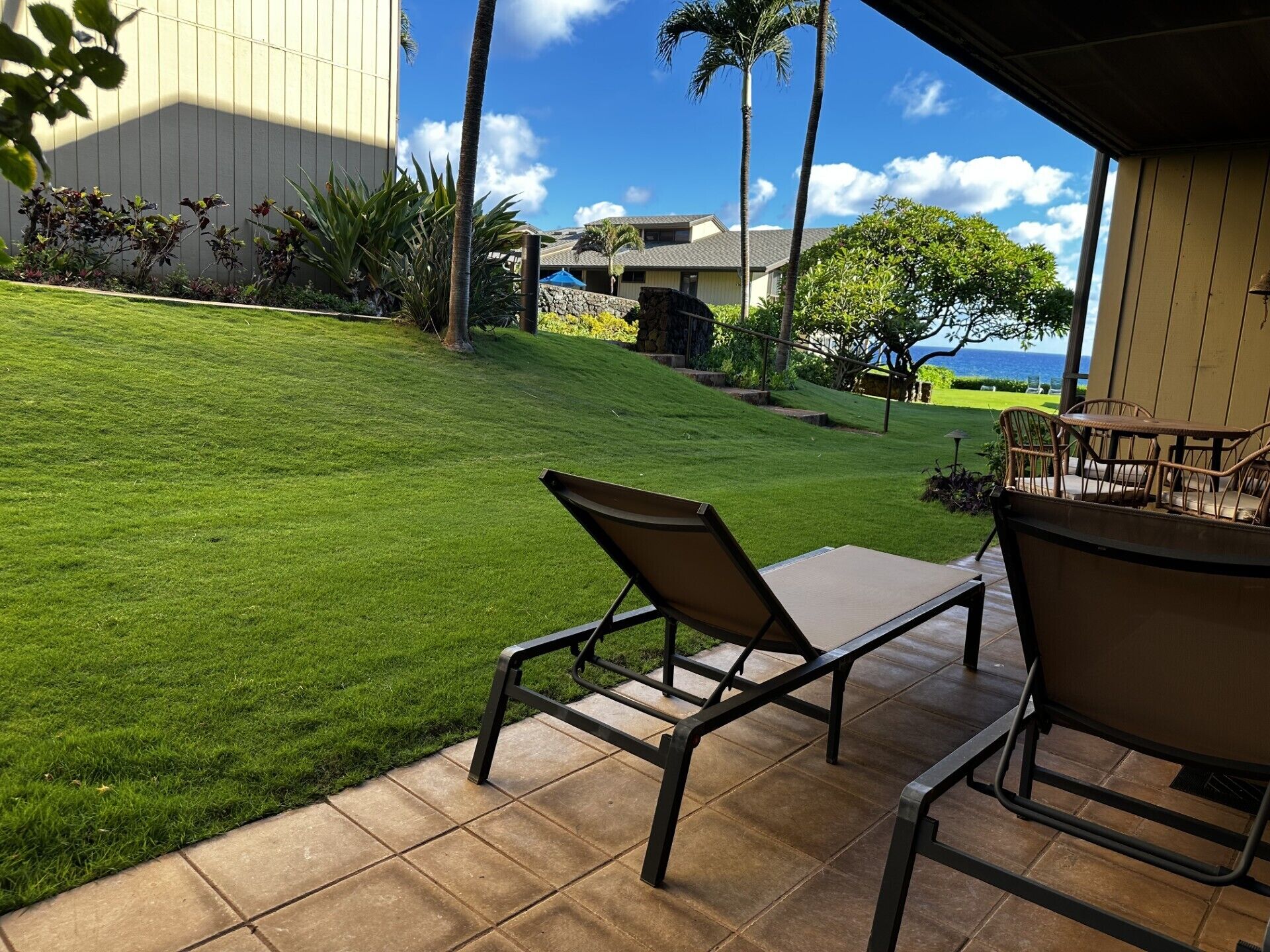 Une terrasse avec deux chaises et une table, une pelouse bien entretenue et une vue sur un immeuble et l’océan.