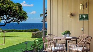 A patio with wicker chairs and a table, overlooking a well-maintained lawn and the ocean.