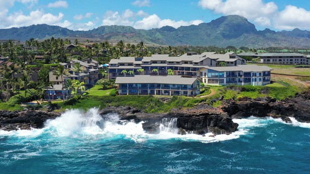 A coastal hotel with multiple buildings, a rocky shoreline, and a mountainous backdrop.