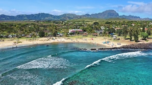 A beach with clear turquoise waters, a sandy shore, and a backdrop of lush green hills and a mountain.