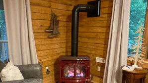 A cozy cabin interior with a wood-burning stove, leather furniture, and a view of trees through a window.