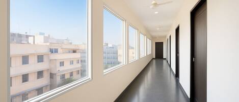 Un pasillo largo y estrecho con amplios ventanales en un lado y puertas en el otro, que conduce a una habitación de color oscuro.