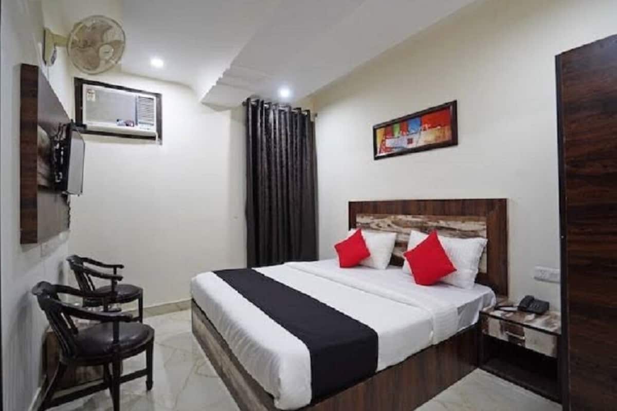 Ein Hotelzimmer mit Bett, Schreibtisch, Stuhl, Ventilator, Klimaanlage und einem Bild an der Wand.