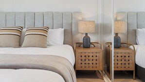 Un dormitorio ordenado con una cama, dos mesitas de noche, un espejo y un cabecero.