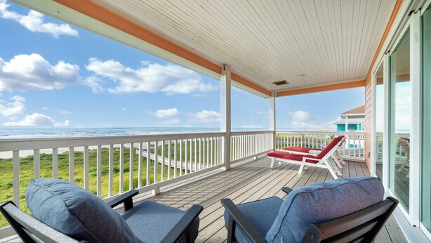 Ein überdachter Außenbereich mit zwei Stühlen und einem Tisch, mit Blick auf Strand und Meer.