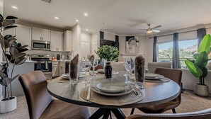 A modern dining room with a round table set for four, surrounded by leather chairs. The room features a kitchen with white cabinets and stainless steel appliances. - Cozy Scottsdale 2BR - 2BA/ Pool/Gym/Free Parking (Scottsdale)