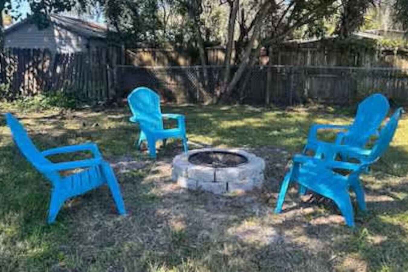 Ein Garten mit Feuerschale und drei blauen Stühlen, die darum platziert sind.