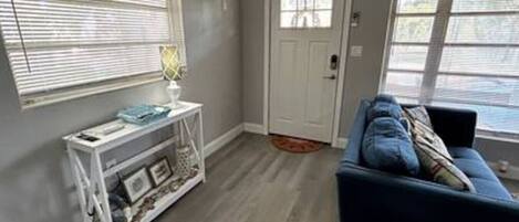 A living room with a blue sofa, a white console table with decorative items, and a door with a window.