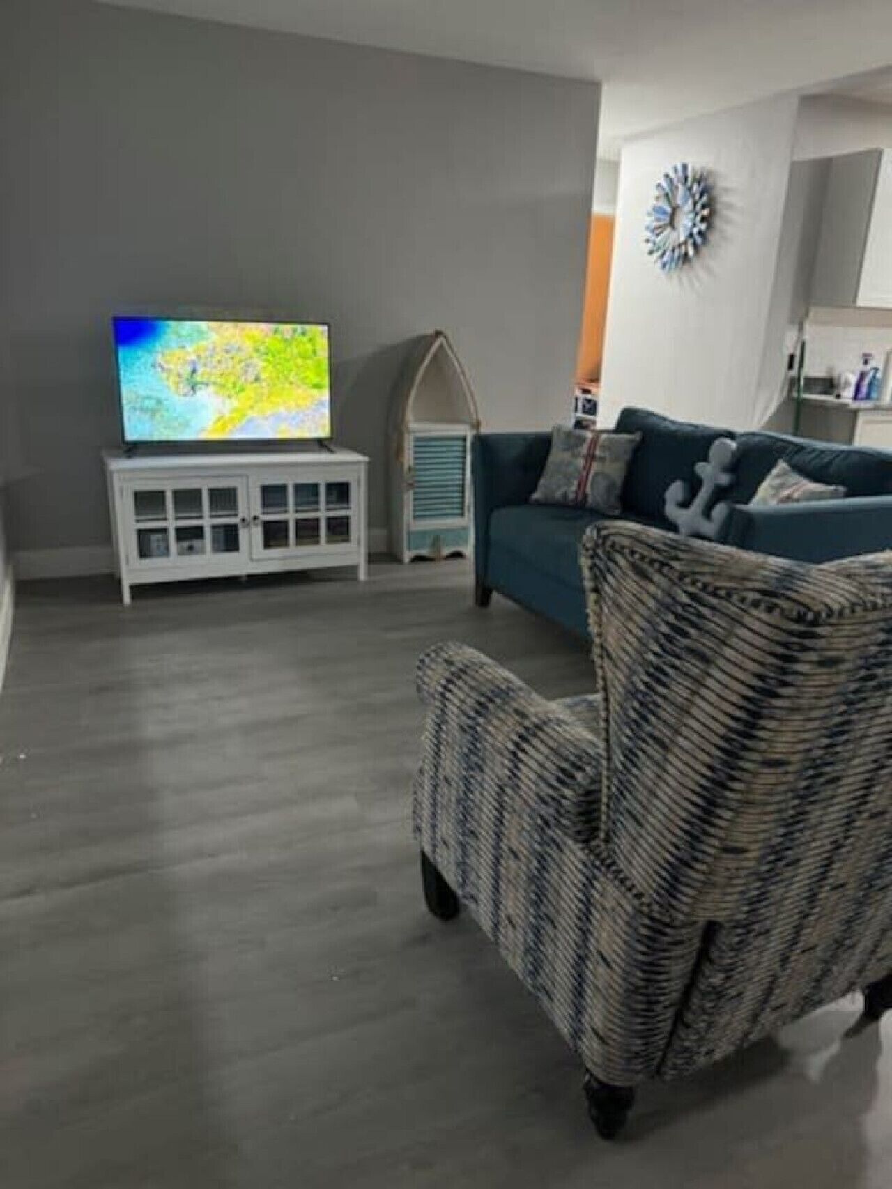 A living room with a television on a white cabinet, a blue sofa with cushions, and a wicker chair.