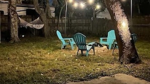 En utomhusplats med sittplatser och en hängmatta under träd, upplyst av ljusslingor.
