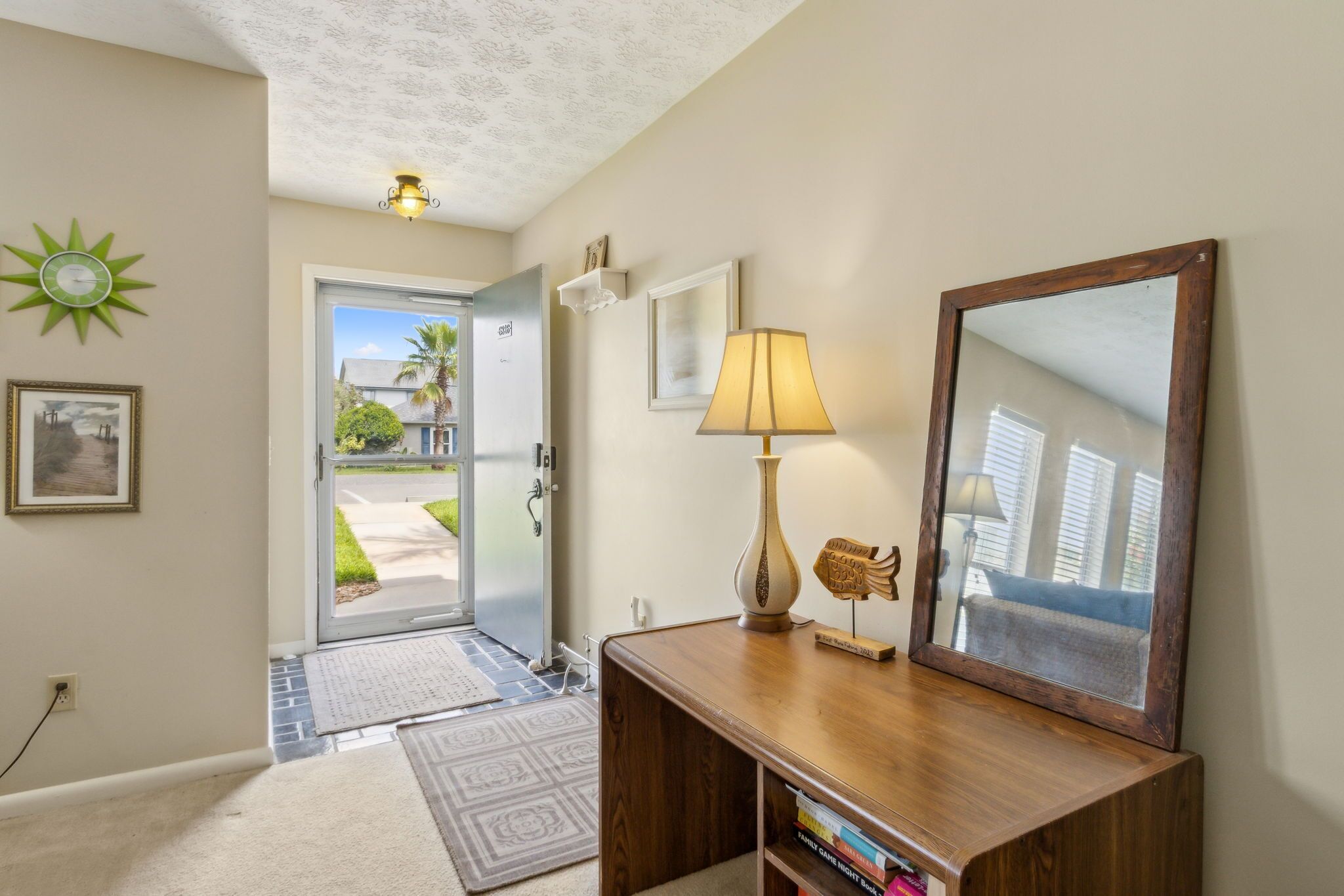 A hallway with a wooden desk, a lamp, a mirror, and a door leading outside.