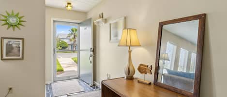 A hallway with a wooden desk, a lamp, a mirror, and a door leading outside.