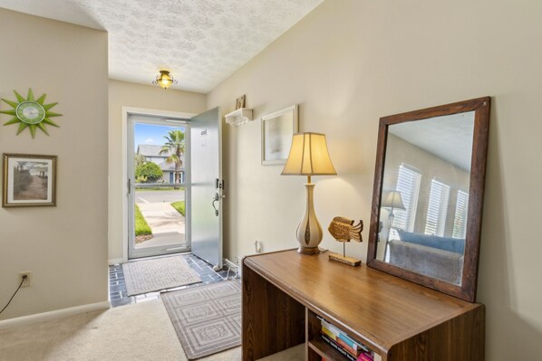 A hallway with a wooden desk, a lamp, a mirror, and a door leading outside.