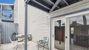 Une terrasse couverte avec une porte-fenêtre coulissante, une petite table, deux chaises et un tuyau bleu enroulé sur la plateforme.