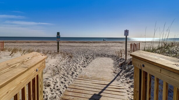 Une promenade en bois menant à une plage, avec un ciel dégagé.