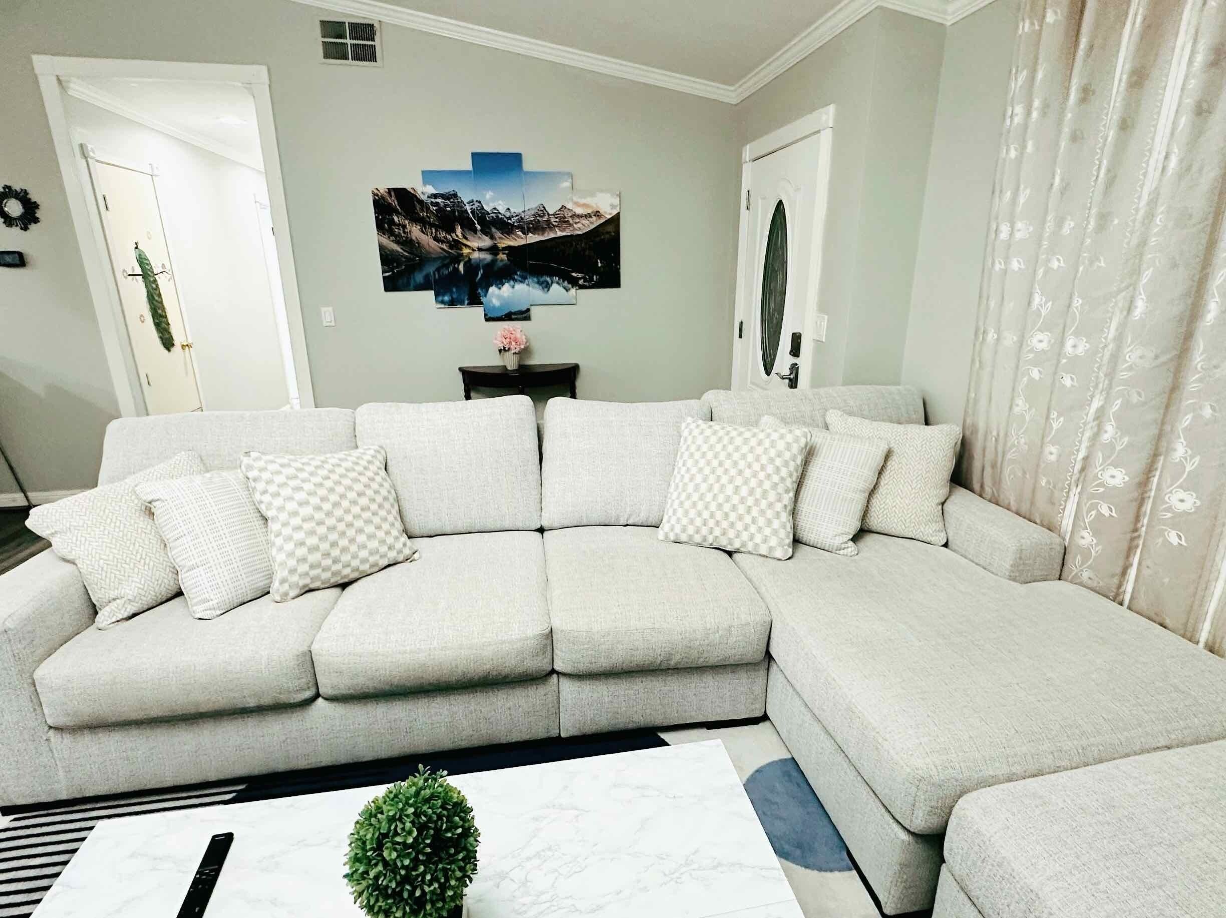 Ein modernes Wohnzimmer mit einer Eckcouch, einem Couchtisch und einem an der Wand befestigten Fernseher.