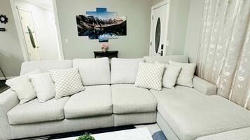 Ein modernes Wohnzimmer mit einer Eckcouch, einem Couchtisch und einem an der Wand befestigten Fernseher.