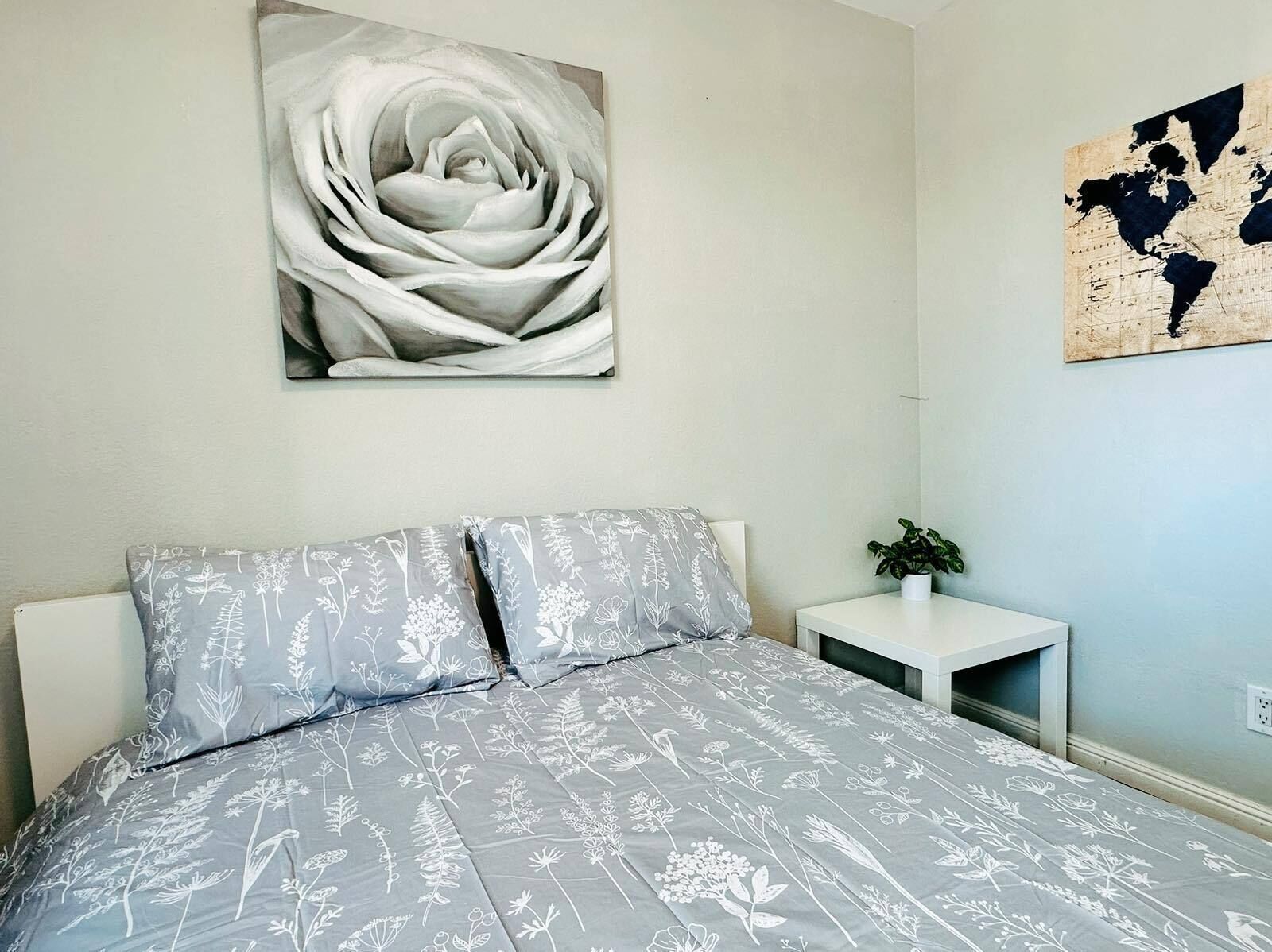 A bedroom with a bed, a nightstand, a world map, and a large floral painting on the wall.