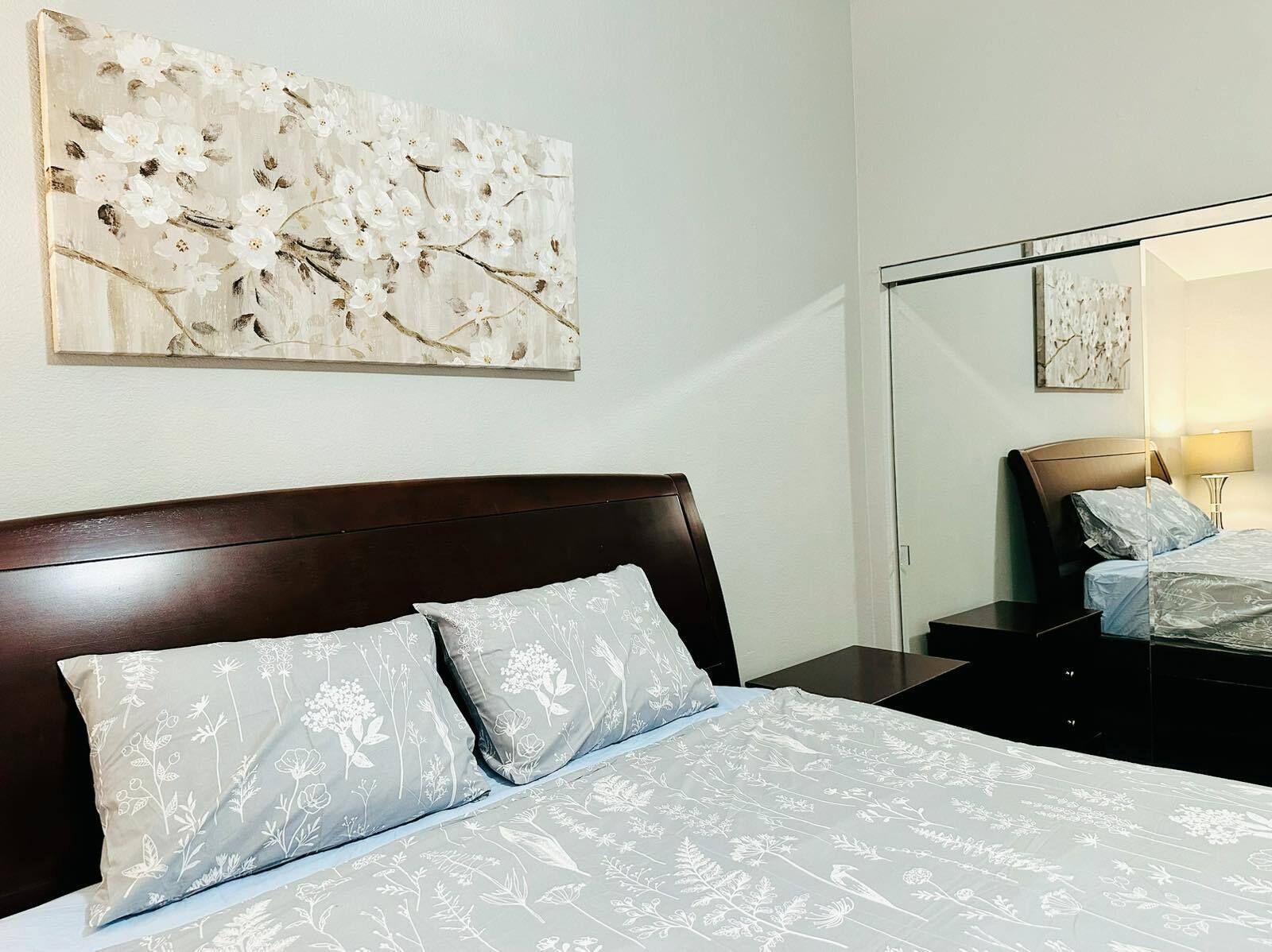 Una habitación de hotel con cama, mesita de noche, espejo y un cuadro grande con motivos florales en la pared.