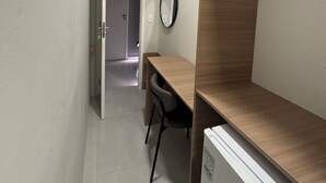 Un estrecho pasillo con un escritorio, una silla, un espejo y una puerta que da a otra habitación.