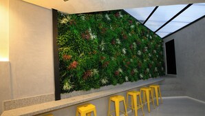 Un interior moderno con un jardín vertical verde, una zona de bar con taburetes amarillos y un tragaluz.