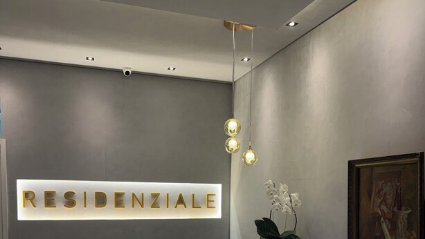 Un área de recepción de diseño moderno, con mostrador de recepción, un letrero en la pared que dice "RESIDENZIALE", iluminación colgante y un cuadro enmarcado.