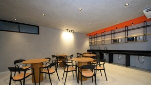 Un café moderno con mesas redondas y sillas negras, que presenta un diseño minimalista y detalles naranja en las paredes.