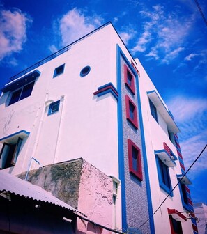 A multi-story building with a white facade and red accents, featuring a series of windows and a visible balcony.