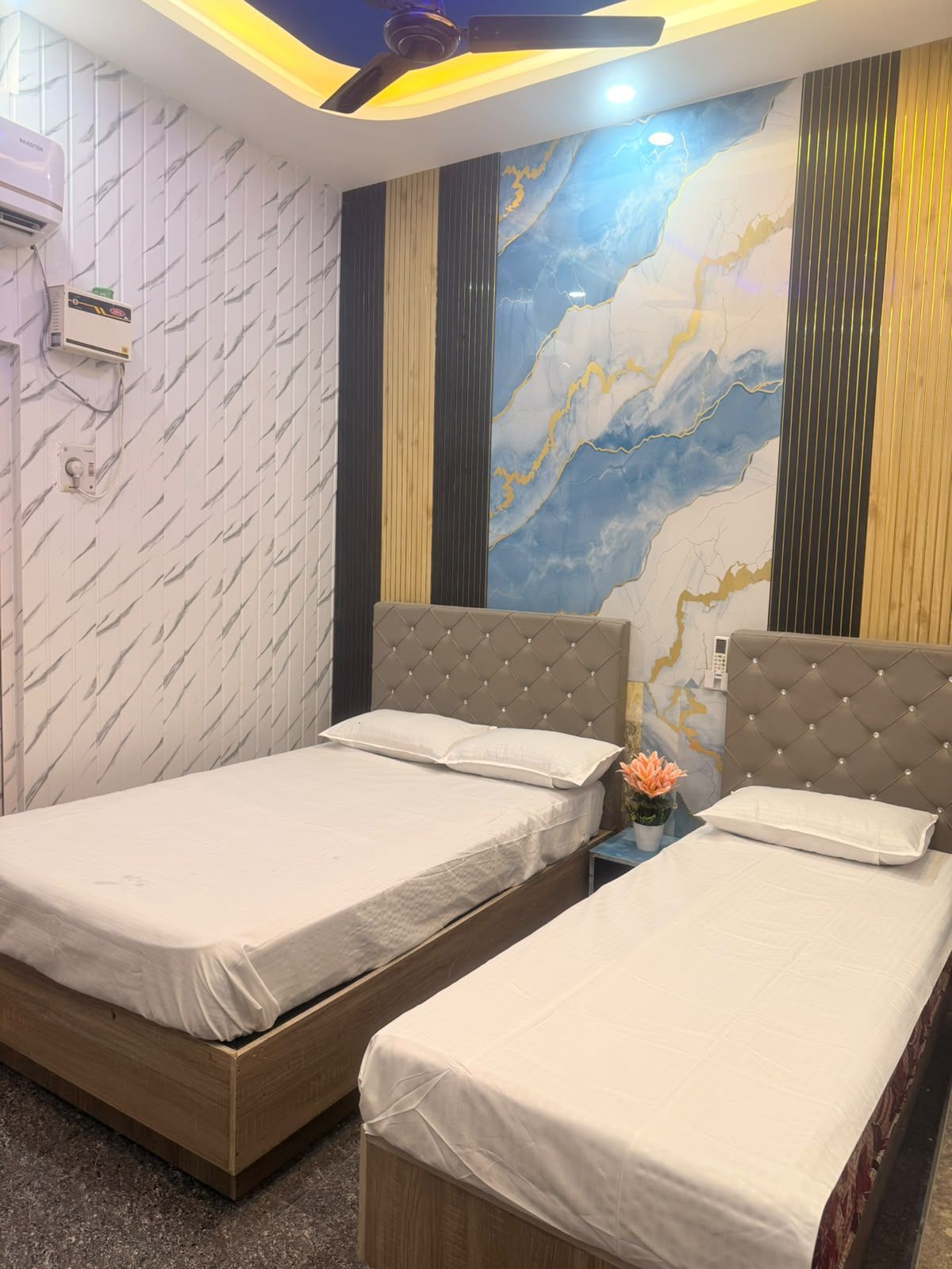 A hotel room with two beds, a marble wall mural, a ceiling fan, and an air conditioning unit.