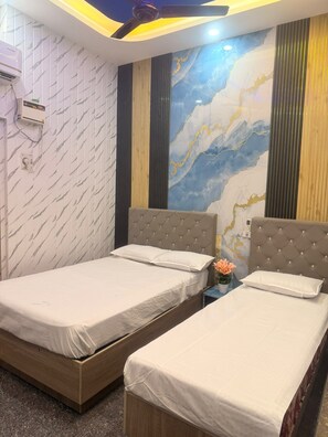 Habitación de hotel con dos camas, un mural de mármol en la pared, ventilador de techo y unidad de aire acondicionado.