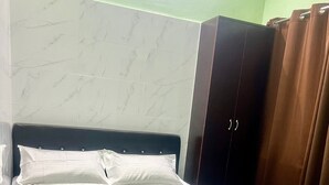 Ein ordentlich bezogenes Bett mit weißer Bettwäsche und einer braunen Decke, ein dunkles Kopfteil und eine Wand mit Marmoroptik im Hintergrund.