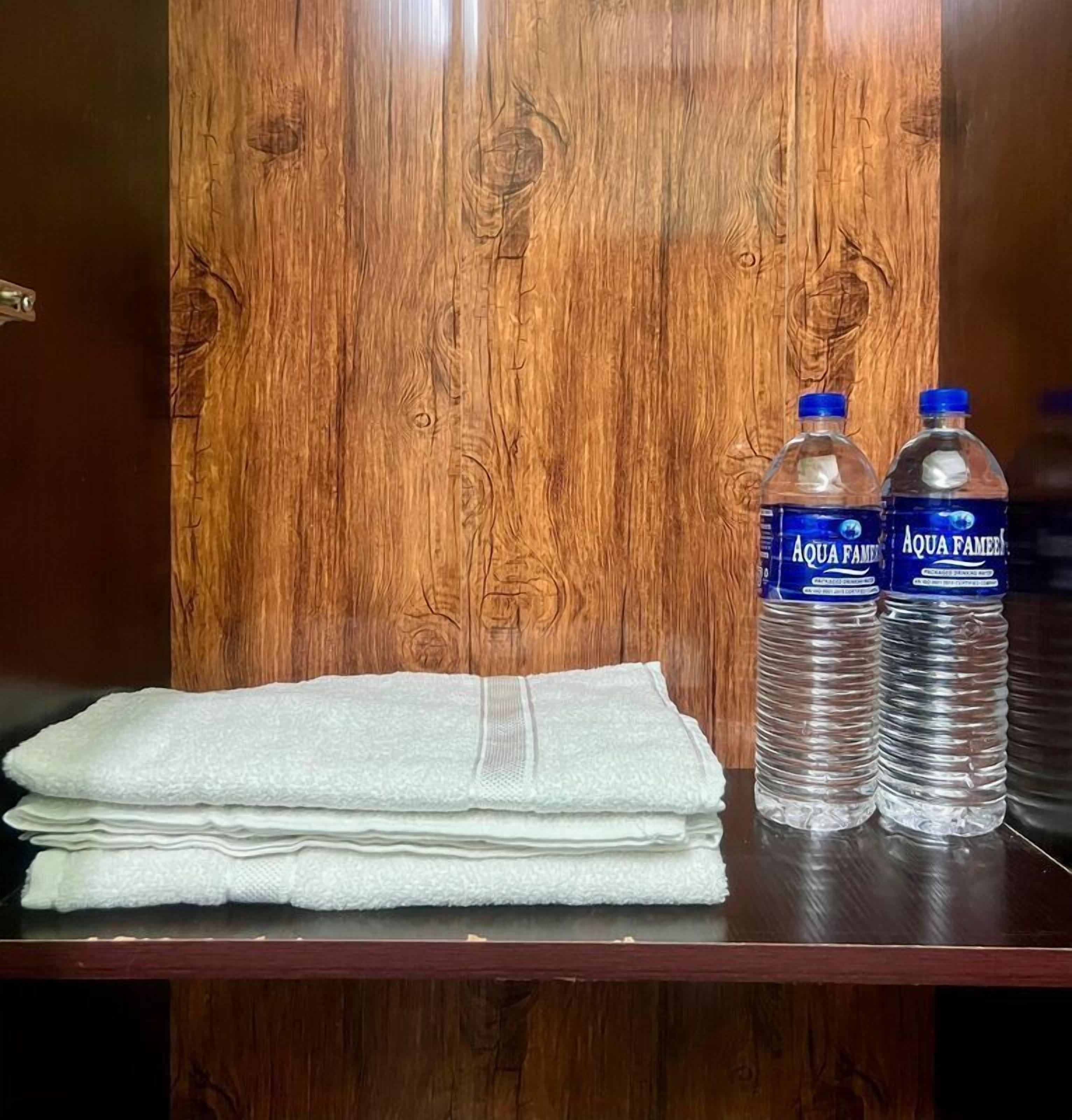 Una pared de madera, dos botellas de agua Aqua Famed y una toalla blanca doblada sobre una mesa.