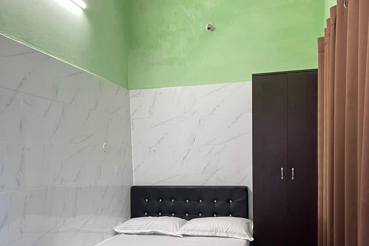 A room with a bed, a wardrobe, and a green and white tiled wall.