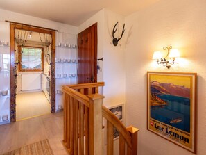 Un escalier avec des rampes en bois mène à un palier. Un tableau encadré représentant un lac et des montagnes est accroché au mur, au-dessus de l’escalier.