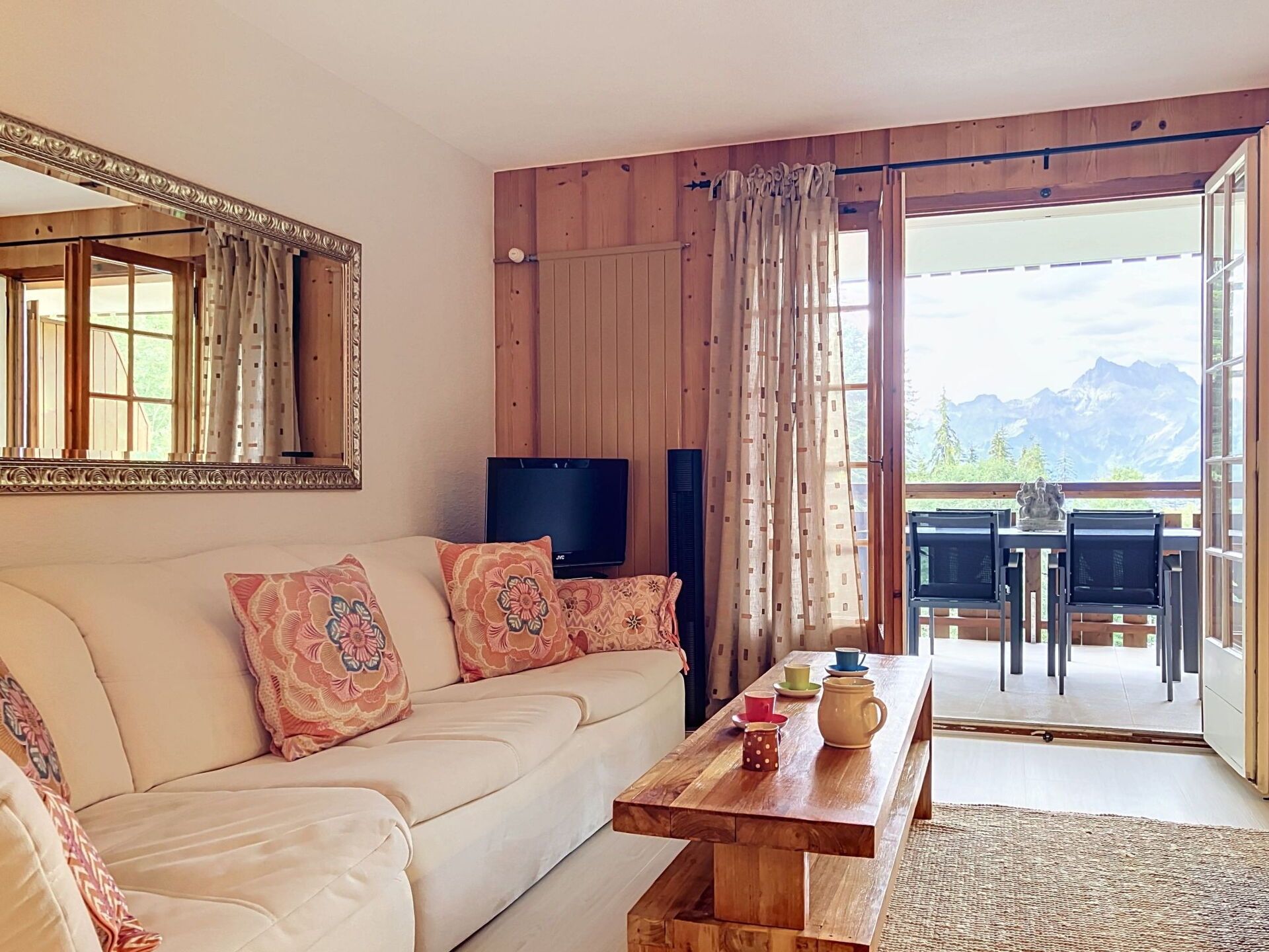 A living room with a sofa, a coffee table, a TV, and a view of mountains through the window.