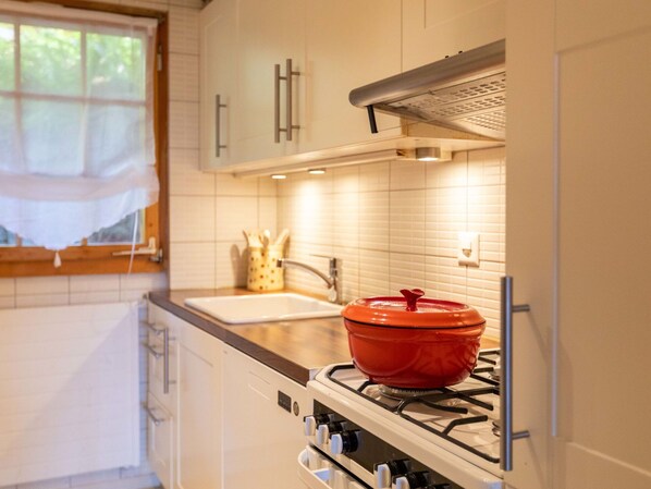 Une cuisine avec des meubles blancs, une cuisinière et une casserole rouge posée sur la cuisinière.