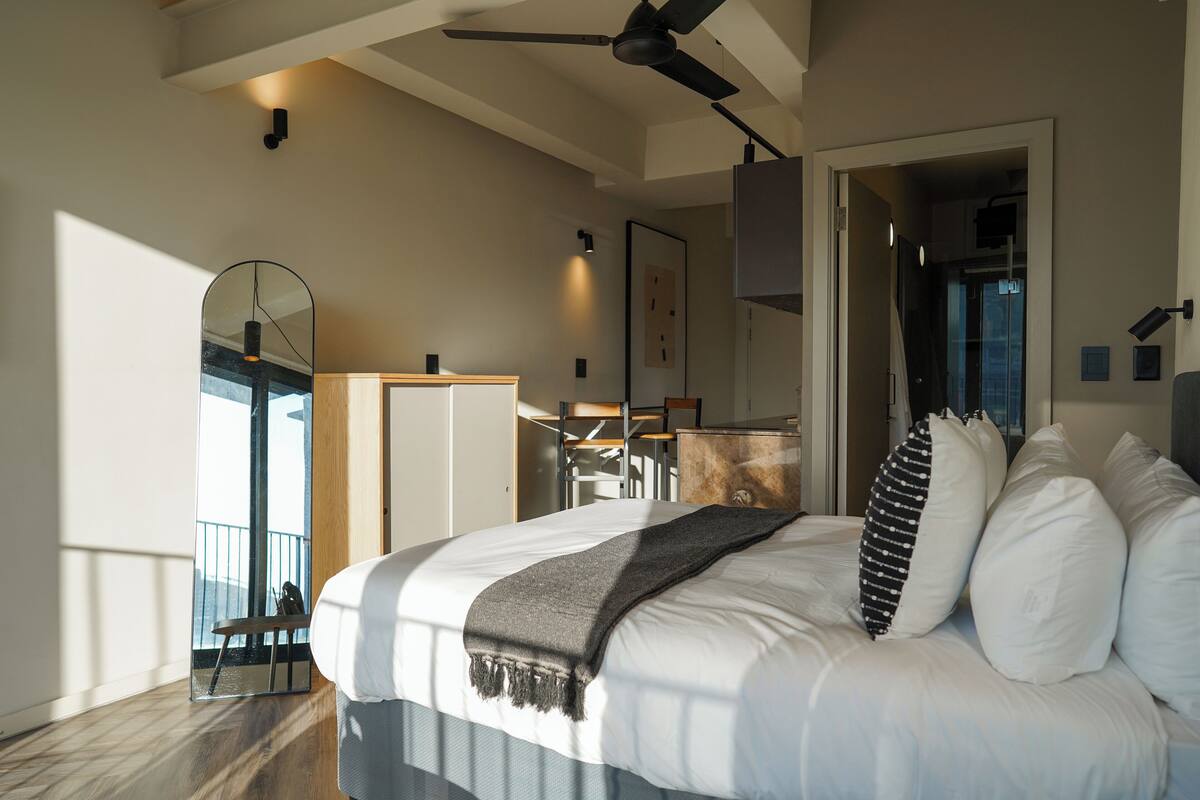A modern bedroom with a large bed, a ceiling fan, and a view of the outdoors.