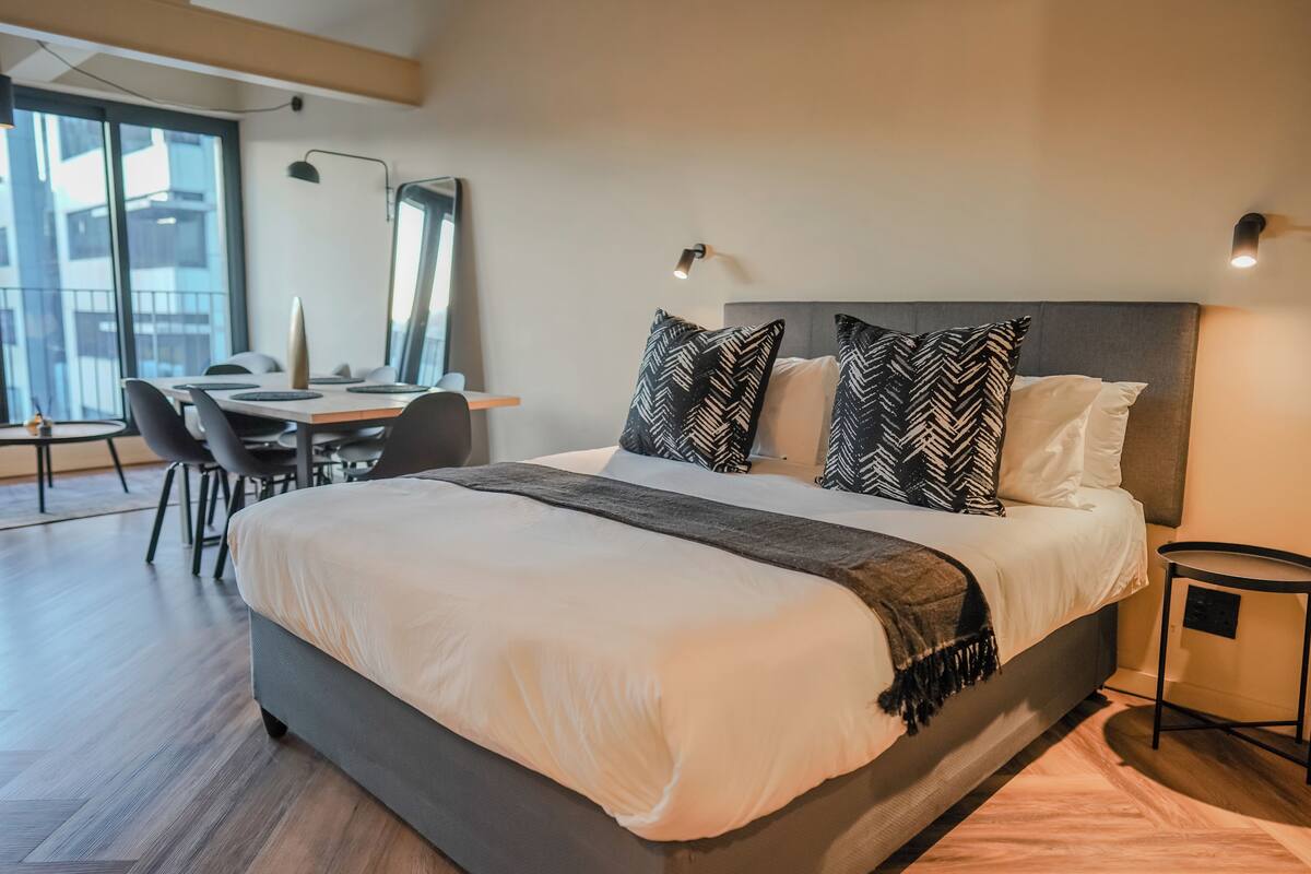 A modern hotel room with a large bed, a desk, and a chair.