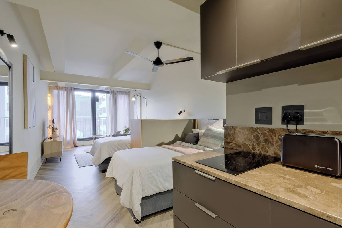 A modern hotel room with a bed, bedside table, and a kitchenette with a Russell Hobbs toaster.