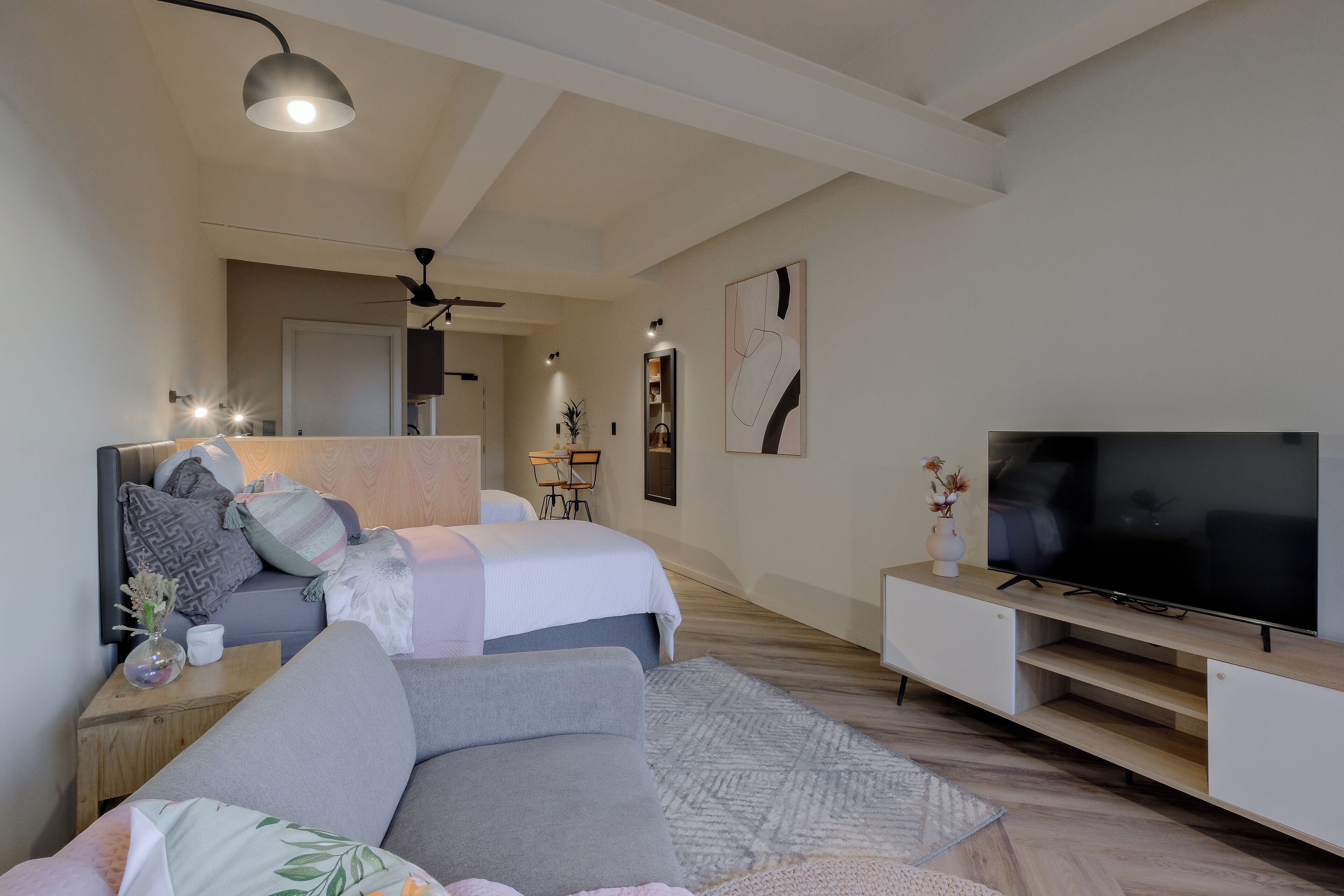 Ein modernes Schlafzimmer mit Bett, einer Couch, einem Fernseher und einem Deckenventilator.