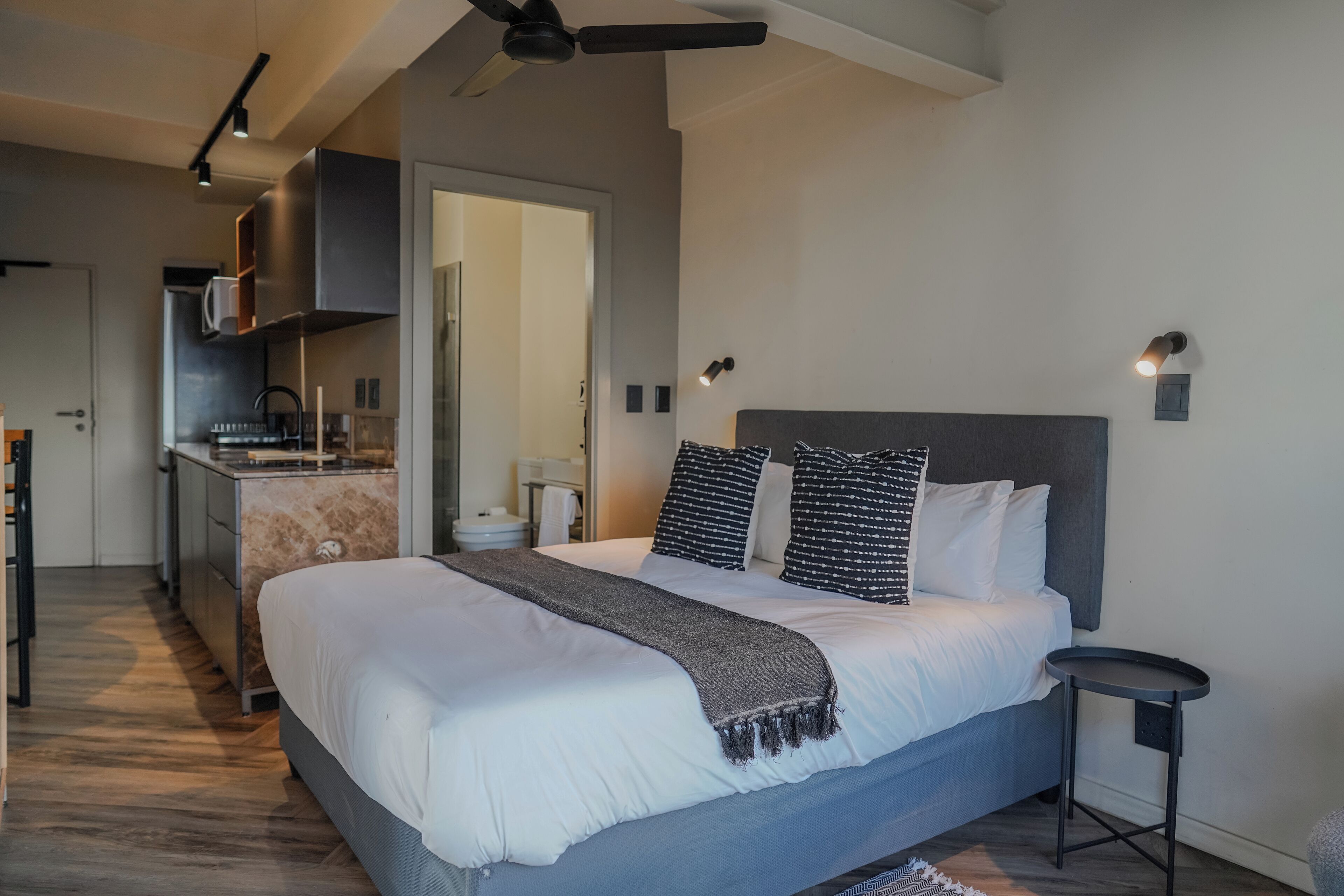 A modern bedroom with a large bed, a small bedside table, and a built-in kitchen area.