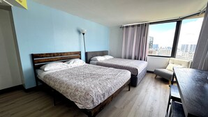 A hotel room with two beds, a desk, a chair, a lamp, and a view of the city.