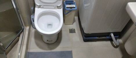 A bathroom with a toilet, a trash bin, and a shower area.