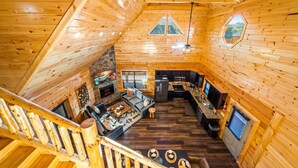 Een chaletinterieur met een stenen openhaard, houten wanden, een keukenhoek en een trap.