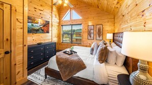 Een slaapkamer in een blokhut met een bed, een dressoir, een plafondventilator en een raam met jaloezieën.