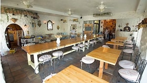A restaurant with a long wooden counter, metal chairs, and a stone wall with decorative elements.