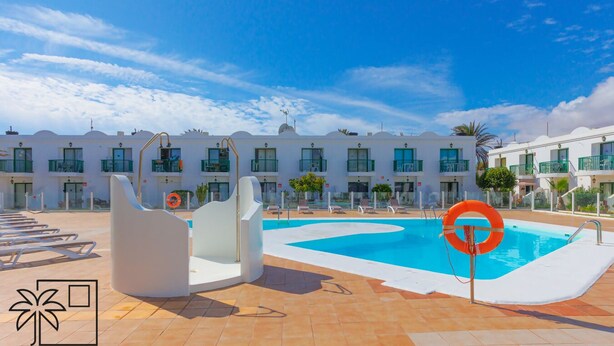 Zona de piscina de hotel con cielo azul despejado, piscina, sillas de descanso y un flotador.
