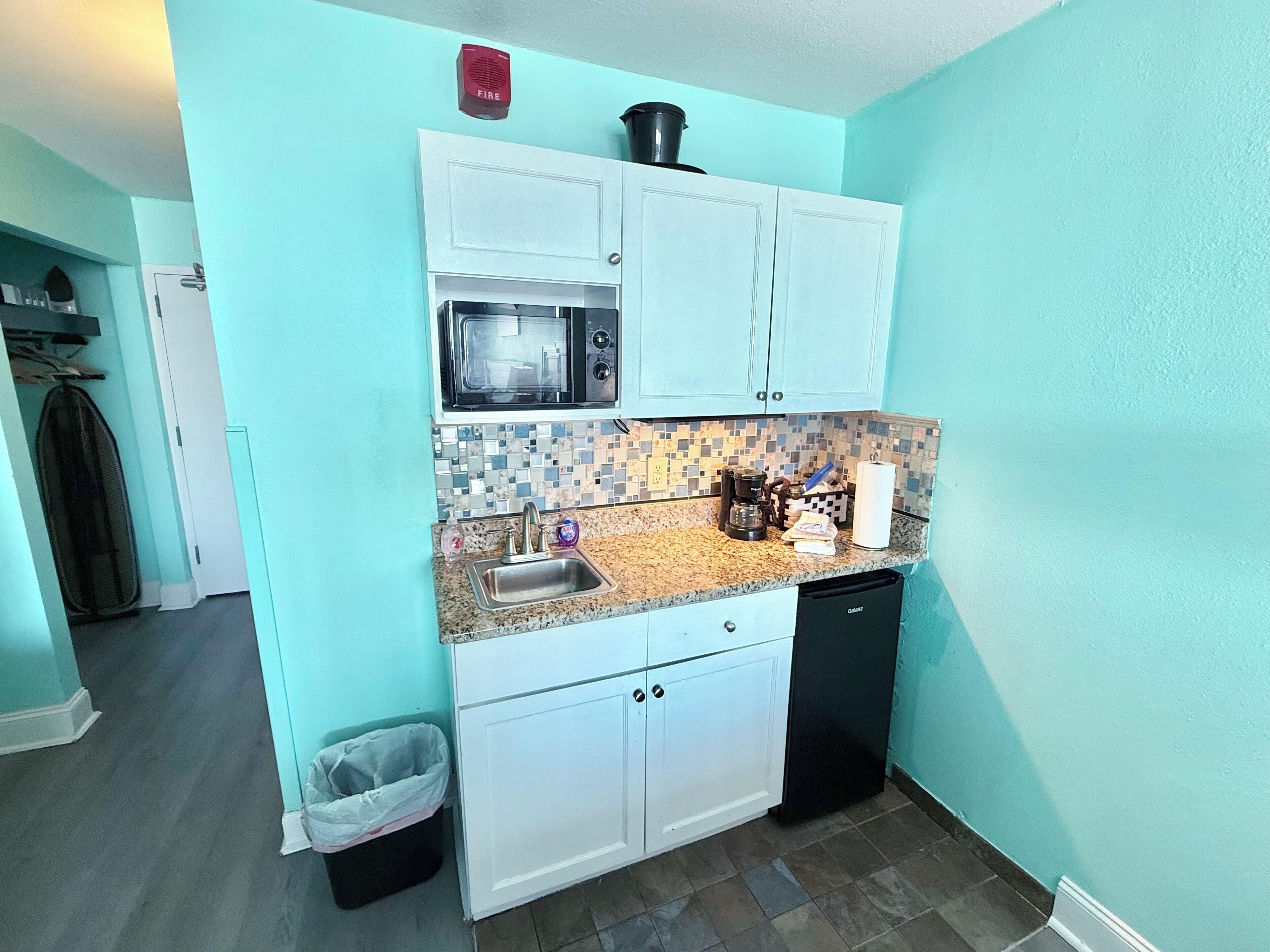 A compact kitchen with white cabinets, a microwave, a coffee maker, and a trash bin.