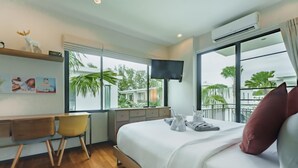 Ein Hotelzimmer mit einem Bett, einem Schreibtisch mit zwei Stühlen, einem Fernseher und einem großen Fenster mit Blick auf Palmen und Gebäude.