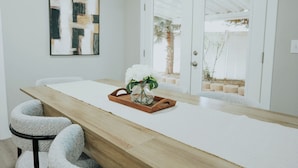Ein moderner Essbereich mit einem Holztisch, weißen Stühlen und einer Vase mit weißen Blumen.